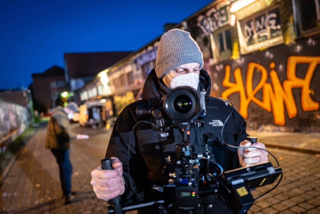 Director of Photography and lecturer at BIMM University Berlin Olaf Markmann while on shoot. He is holding a large camera and looking into the monitor.