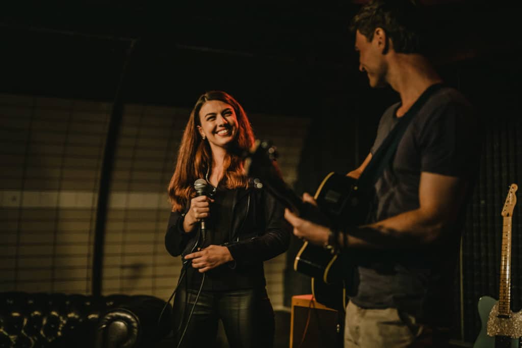 One woman holding a microphone, 1 man holding a guitar