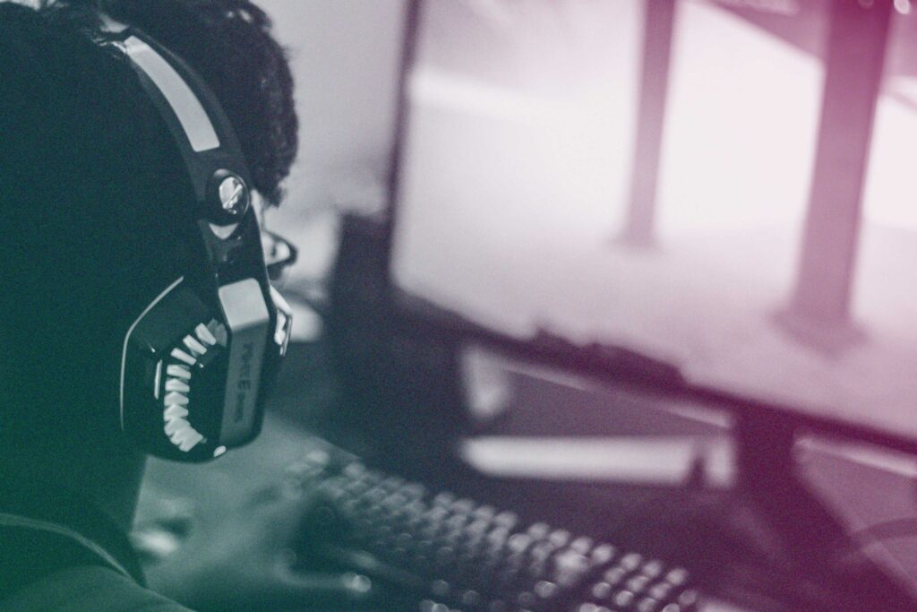A student wearing gaming headphones looks towards a computer screen.